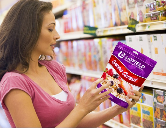 Woman in a grocery aisle examining a resealable pouch of granola cereal with Layfield branding.