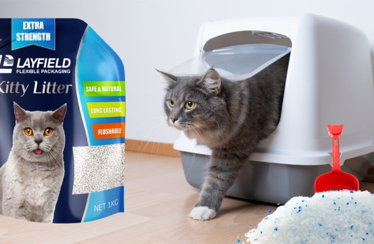 Gray cat exiting a litter box beside a flexible package of cat litter labeled safe, natural, long lasting, and flushable.