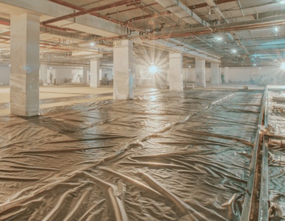 Commercial construction site with heavy-duty plastic sheeting installed for moisture protection and underslab vapor barrier application.