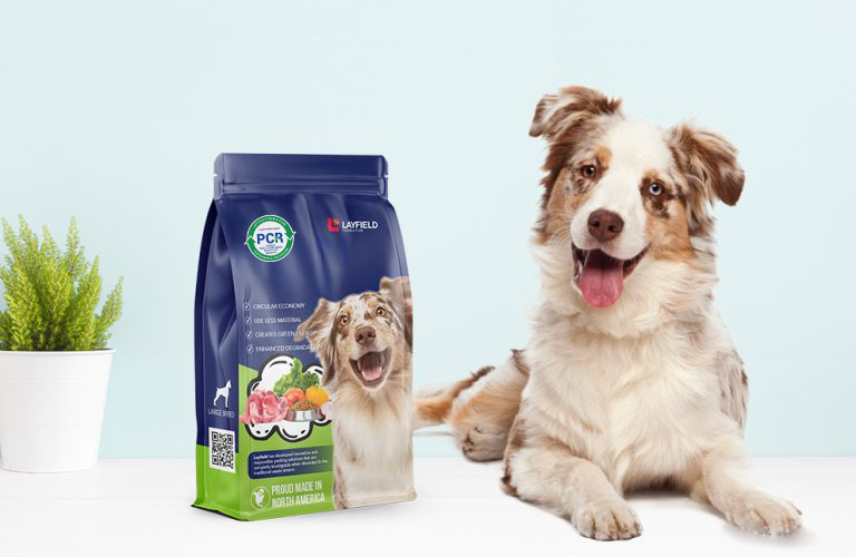 Dog sitting beside a resealable dry dog food bag made with PCR content, placed on a light blue background.