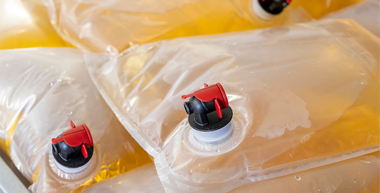 Close-up of industrial liquid food bags with red and black dispensing spouts, filled and stacked for bulk use.