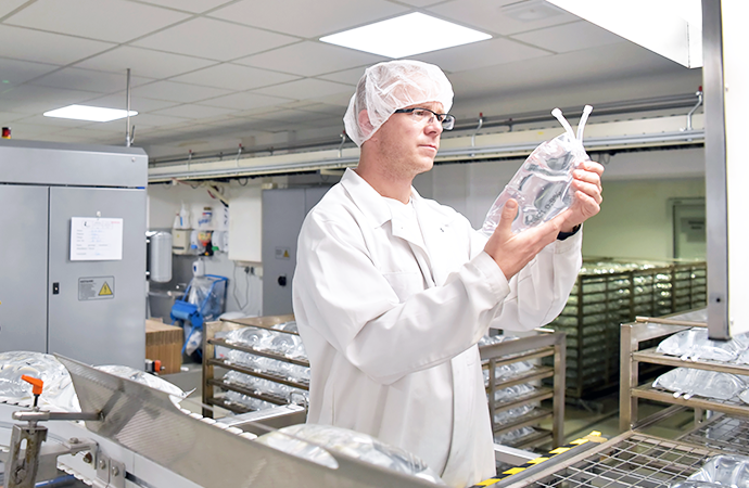 Technician in cleanroom inspecting a formed medical fluid bag for quality assurance