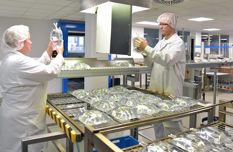 Technicians inspecting medical fluid bags on a cleanroom production line