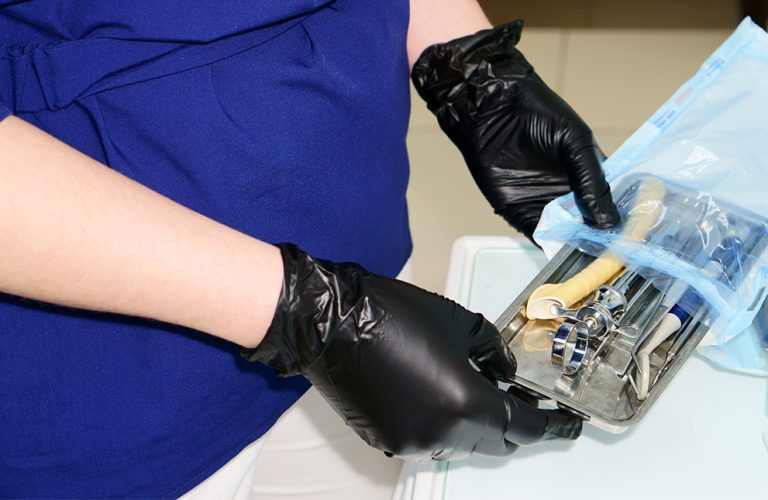 Gloved hands handling sterilized dental instruments on a stainless-steel tray.
