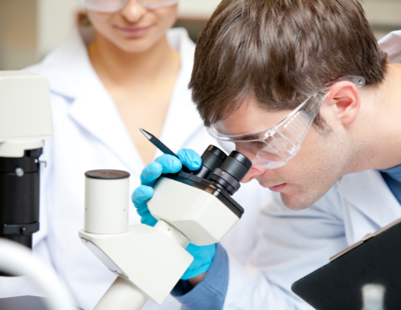 Scientist in protective eyewear examining samples through a microscope