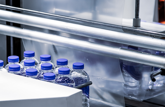 Plastic water bottles on a production line entering shrink film wrapping machinery