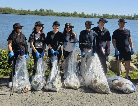 Group of volunteers holding bags of collected litter during an Ocean Wise shoreline cleanup by the water on a sunny day.