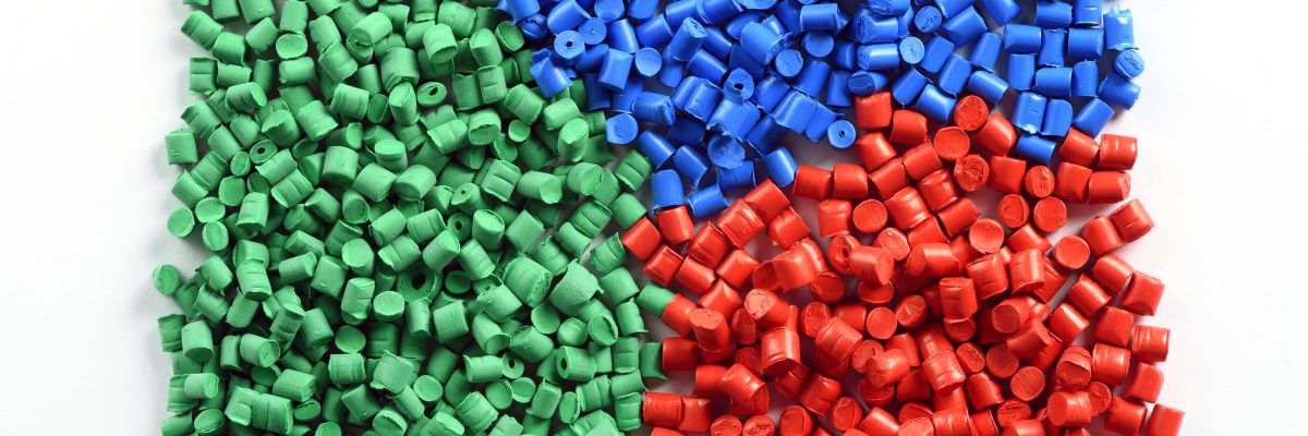 Green, blue, and red plastic pellets organized by color, used in resin-based flexible packaging production.