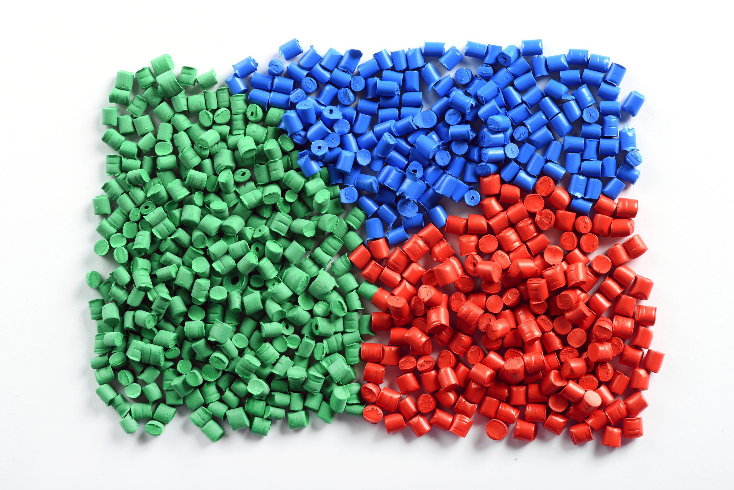 Green, blue, and red plastic pellets organized by color, used in resin-based flexible packaging production.